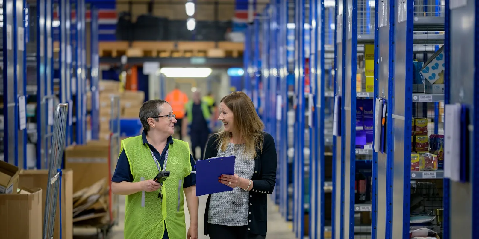 Two colleagues with a clipboard and scanner walking a warehouse aisle