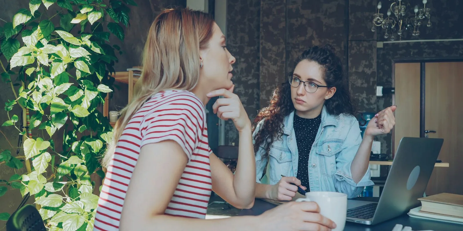 Two women talking through a question over a laptop and coffee