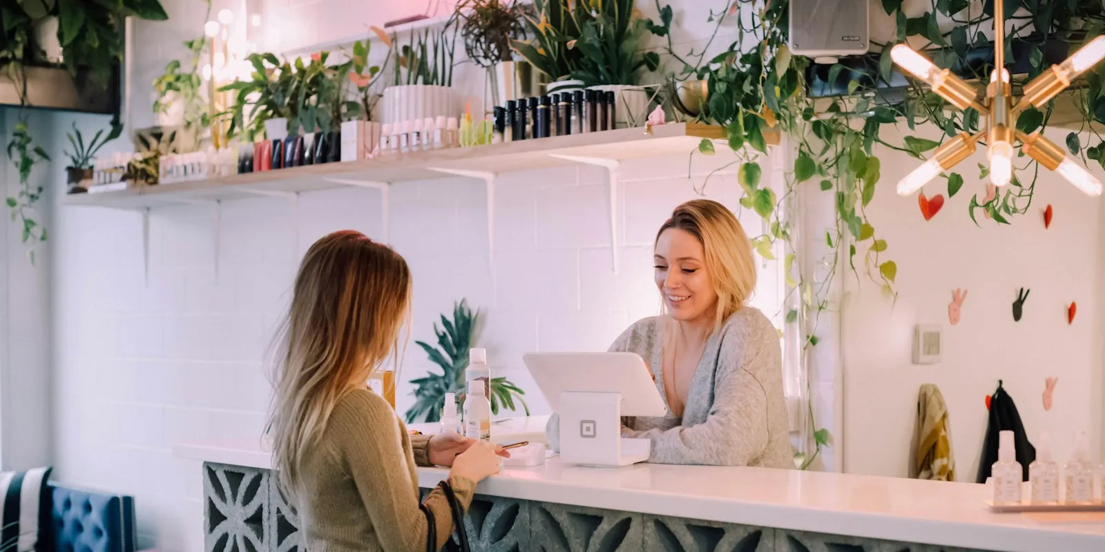 A shop owner serving a customer at the counter of a small plant-filled store