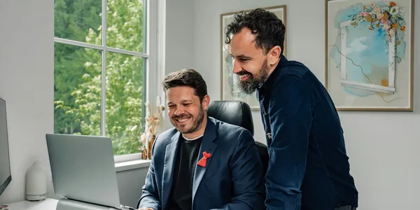 Two colleagues smiling at a laptop while working through a task at a desk