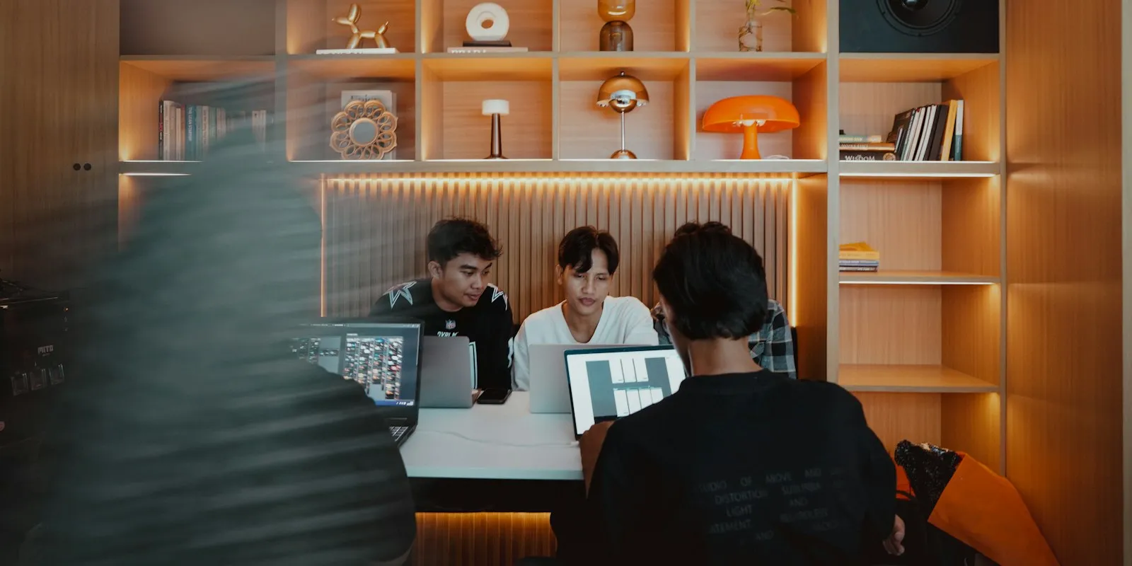 A small team working on laptops in a warm, compact studio